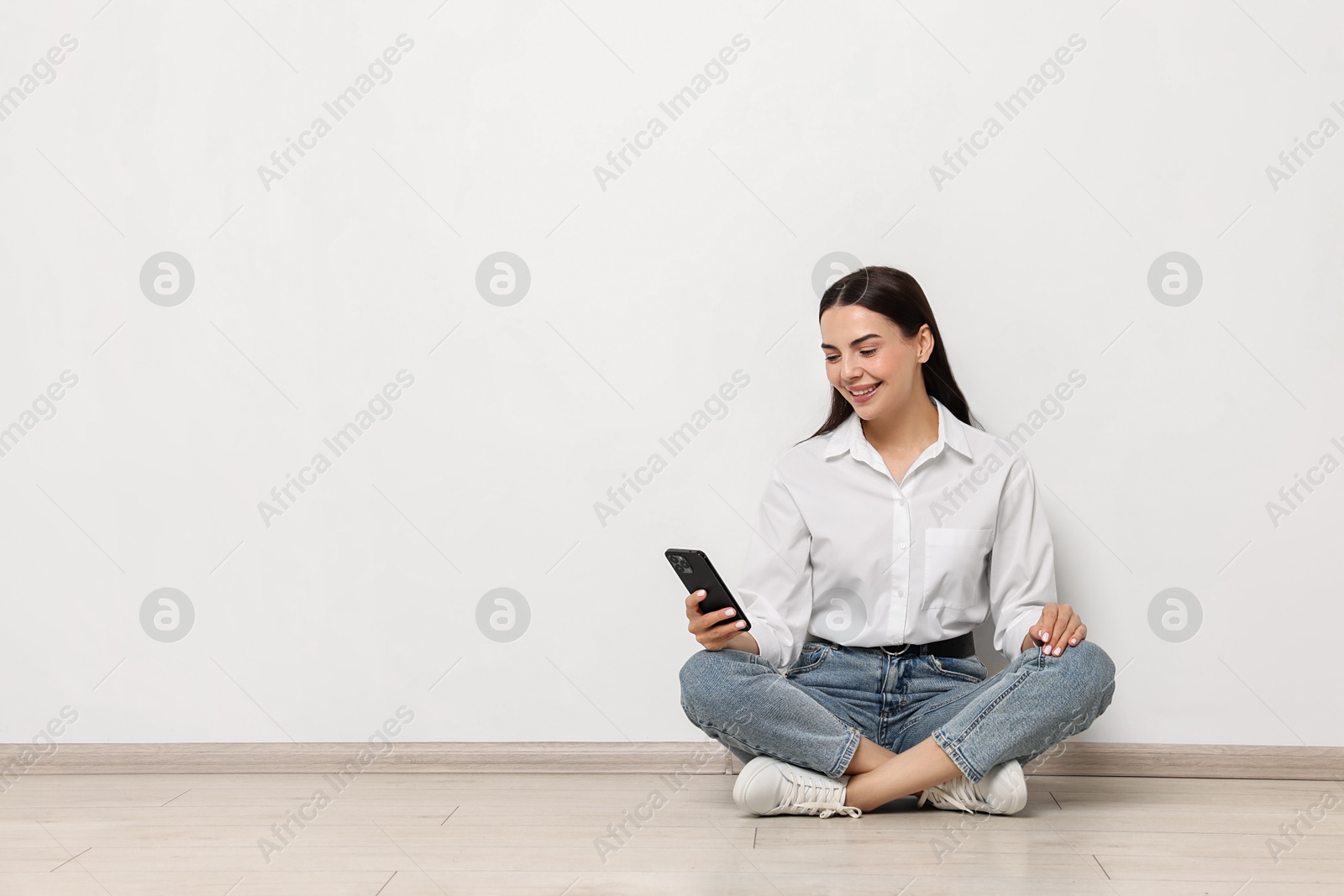 Photo of Smiling woman with smartphone on floor against white background. Space for text