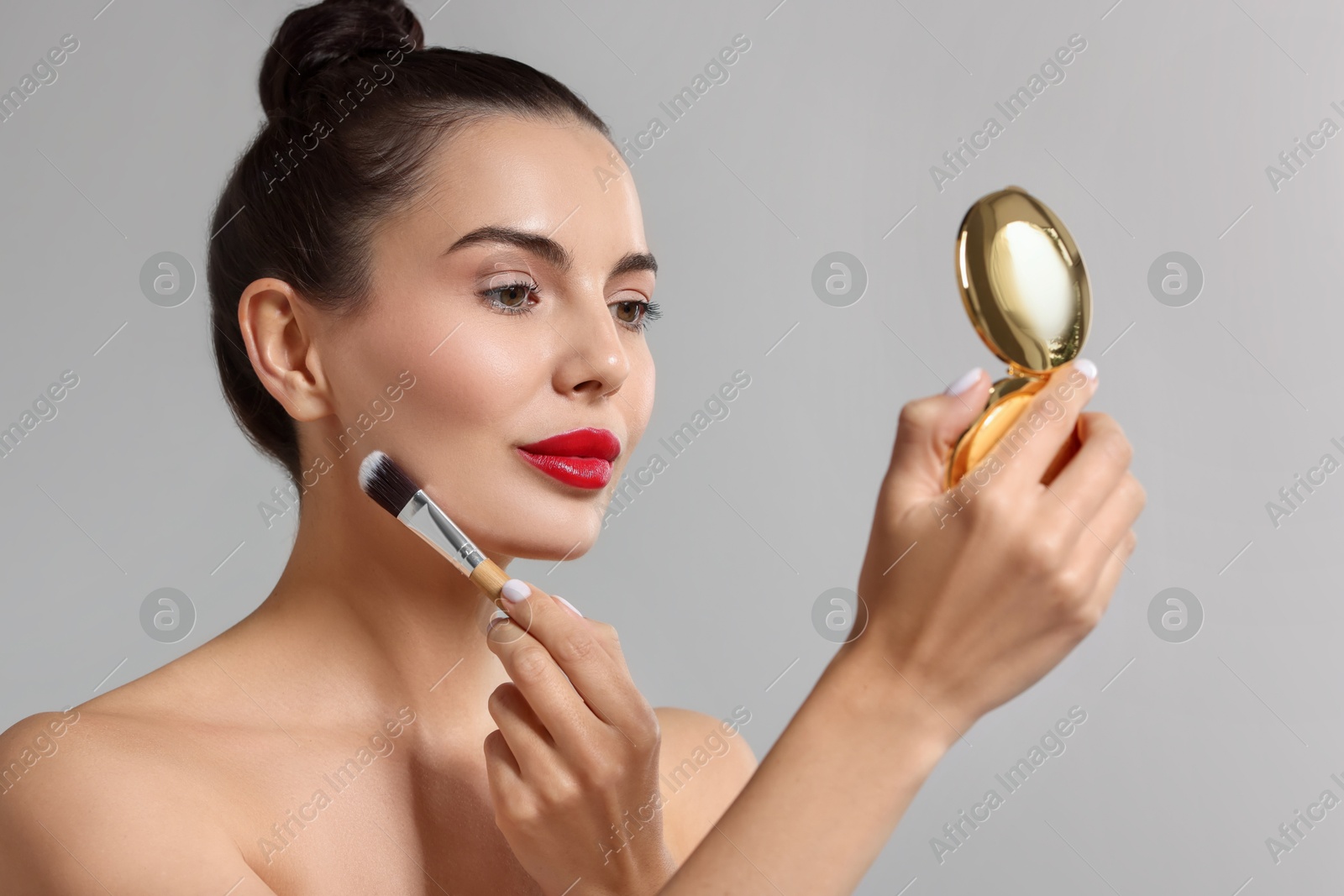 Photo of Beautiful woman with cosmetic product applying makeup on light grey background