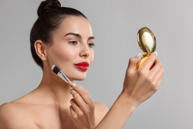 Beautiful woman with cosmetic product applying makeup on light grey background