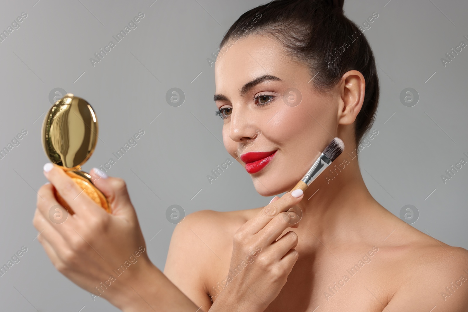 Photo of Beautiful woman with cosmetic product applying makeup on light grey background