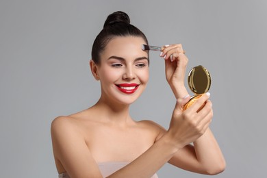 Smiling woman with cosmetic product applying makeup on light grey background