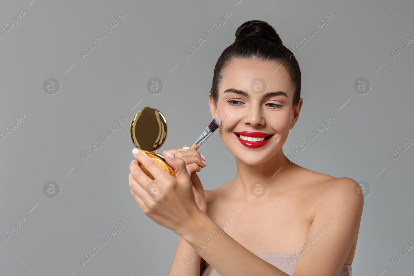 Photo of Smiling woman with cosmetic product applying makeup on light grey background. Space for text