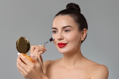 Photo of Beautiful woman with cosmetic product applying makeup on light grey background