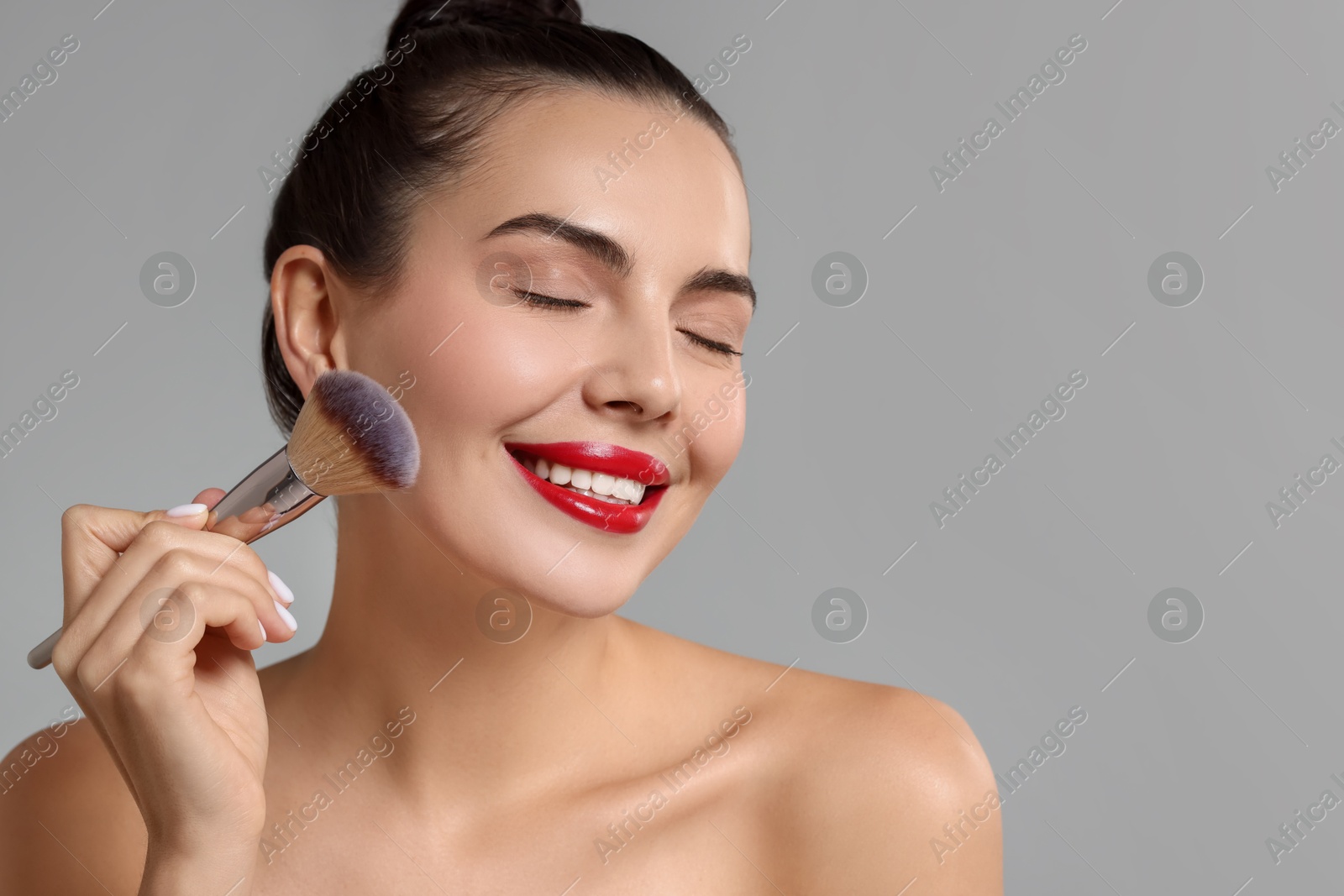 Photo of Smiling woman applying makeup with brush on light grey background. Space for text