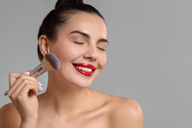 Smiling woman applying makeup with brush on light grey background. Space for text