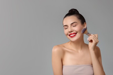 Photo of Smiling woman applying makeup with brush on light grey background. Space for text