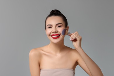 Photo of Smiling woman applying makeup with brush on light grey background