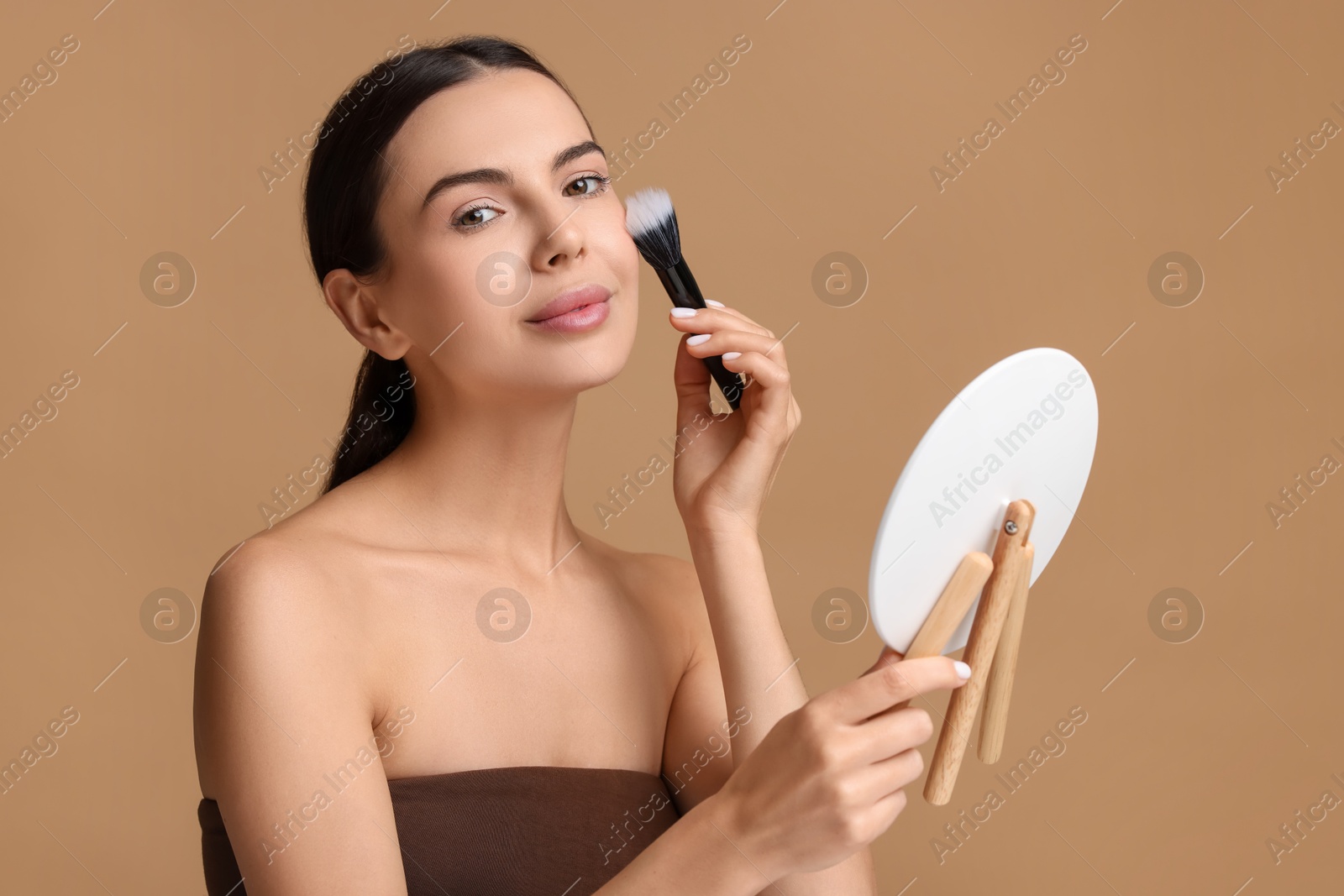 Photo of Beautiful woman with mirror applying makeup on beige background