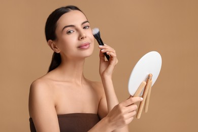 Beautiful woman with mirror applying makeup on beige background