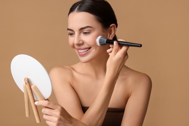 Photo of Beautiful woman with mirror applying makeup on beige background