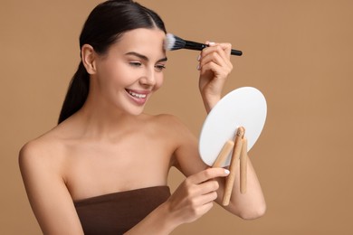 Photo of Beautiful woman with mirror applying makeup on beige background