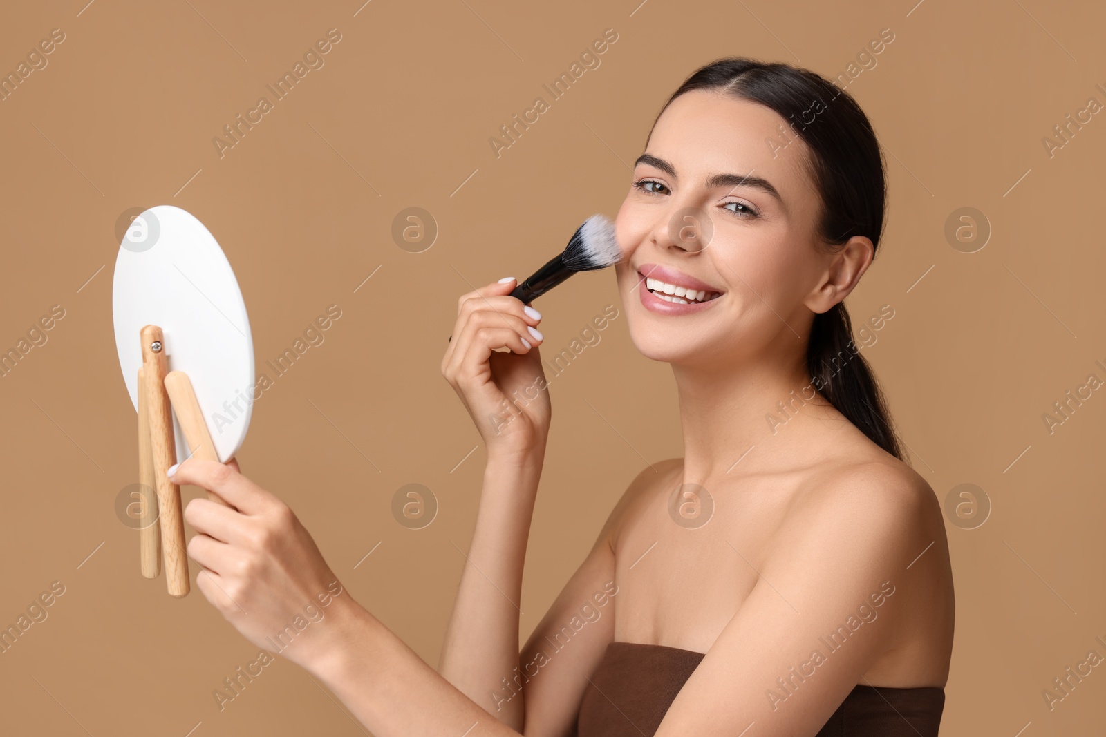 Photo of Beautiful woman with mirror applying makeup on beige background