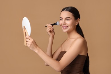 Photo of Beautiful woman with mirror applying makeup on beige background