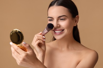 Smiling woman with cosmetic product applying makeup on beige background