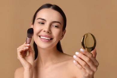 Smiling woman with cosmetic product applying makeup on beige background