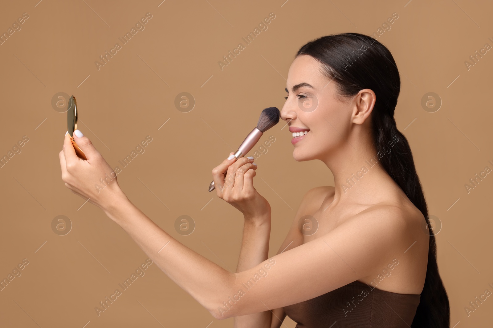 Photo of Smiling woman with cosmetic product applying makeup on beige background