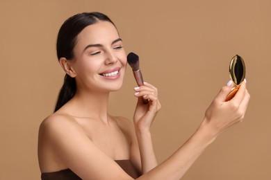 Smiling woman with cosmetic product applying makeup on beige background