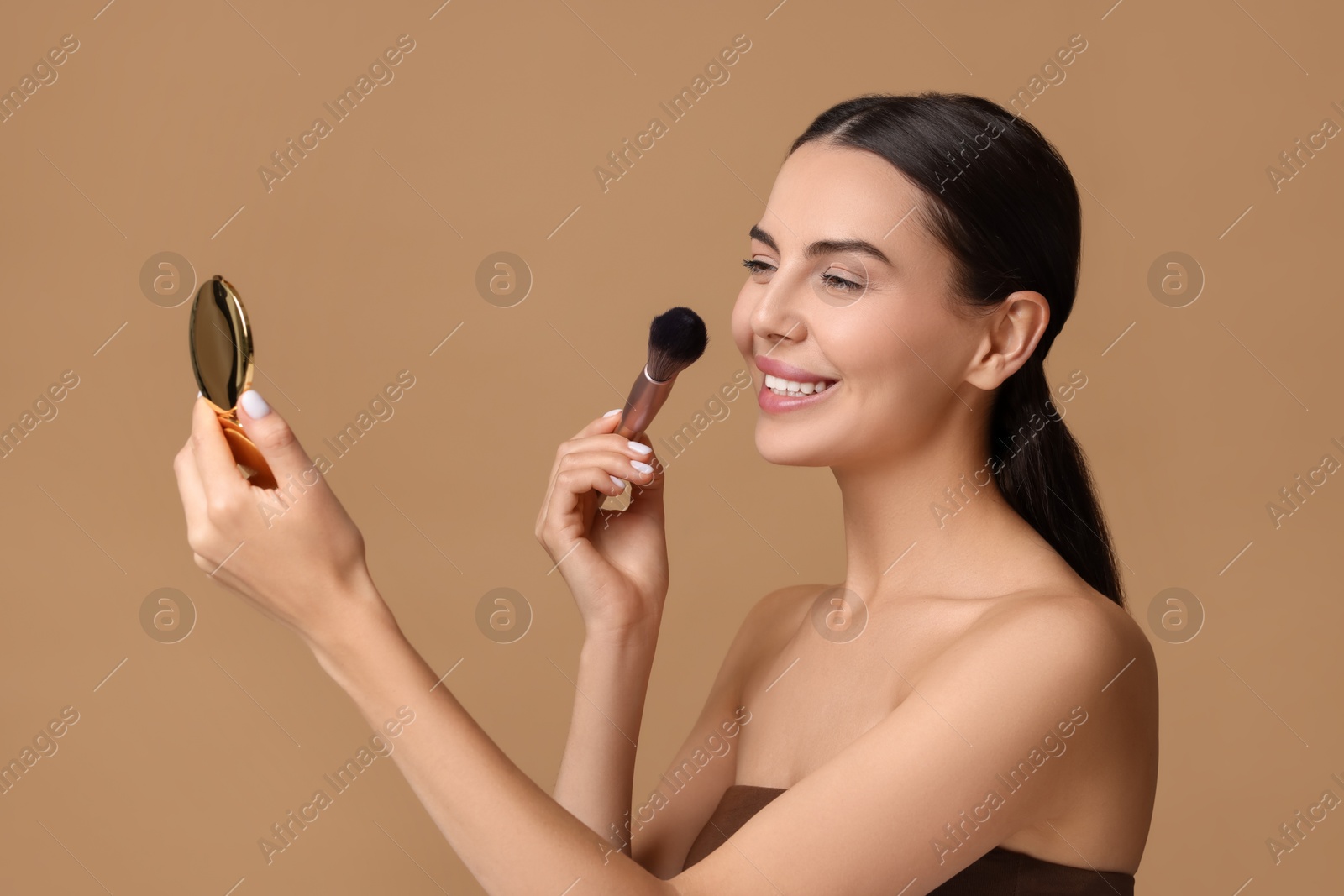 Photo of Smiling woman with cosmetic product applying makeup on beige background