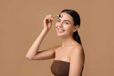 Photo of Smiling woman applying makeup with brush on beige background