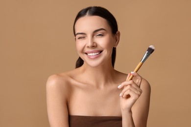 Beautiful makeup. Smiling woman with brush on beige background