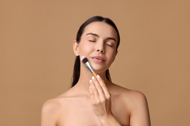 Beautiful woman applying makeup with brush on beige background