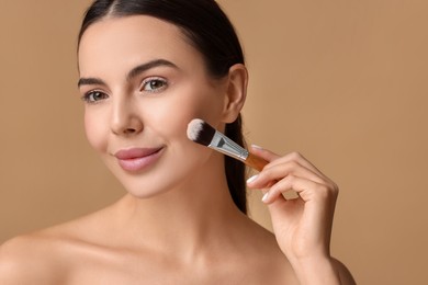 Beautiful woman applying makeup with brush on beige background