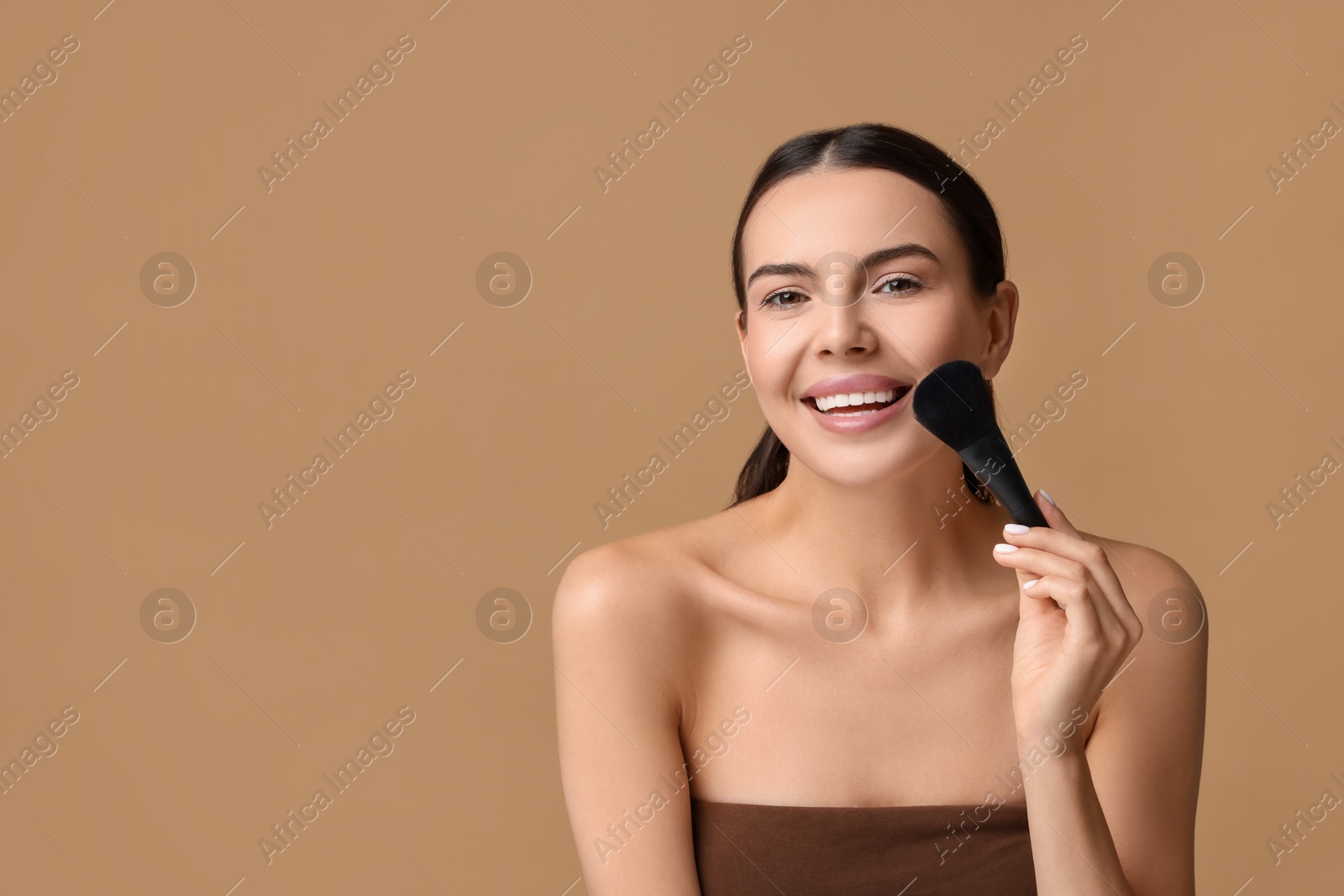 Photo of Smiling woman applying makeup with brush on beige background. Space for text