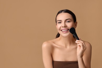 Smiling woman applying makeup with brush on beige background. Space for text