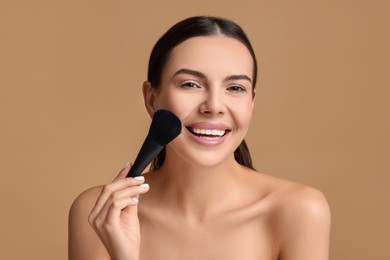 Smiling woman applying makeup with brush on beige background