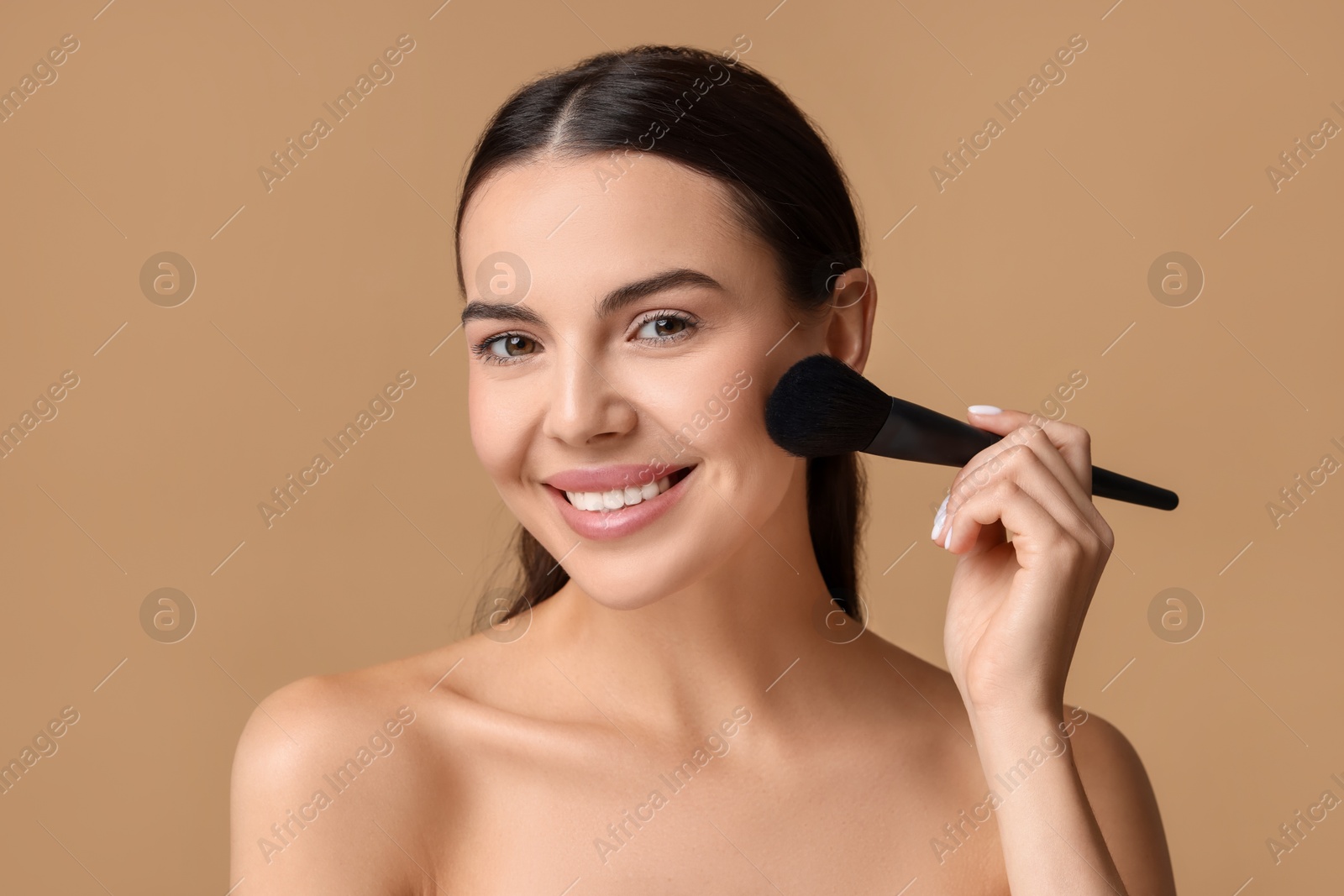 Photo of Smiling woman applying makeup with brush on beige background