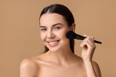 Photo of Smiling woman applying makeup with brush on beige background