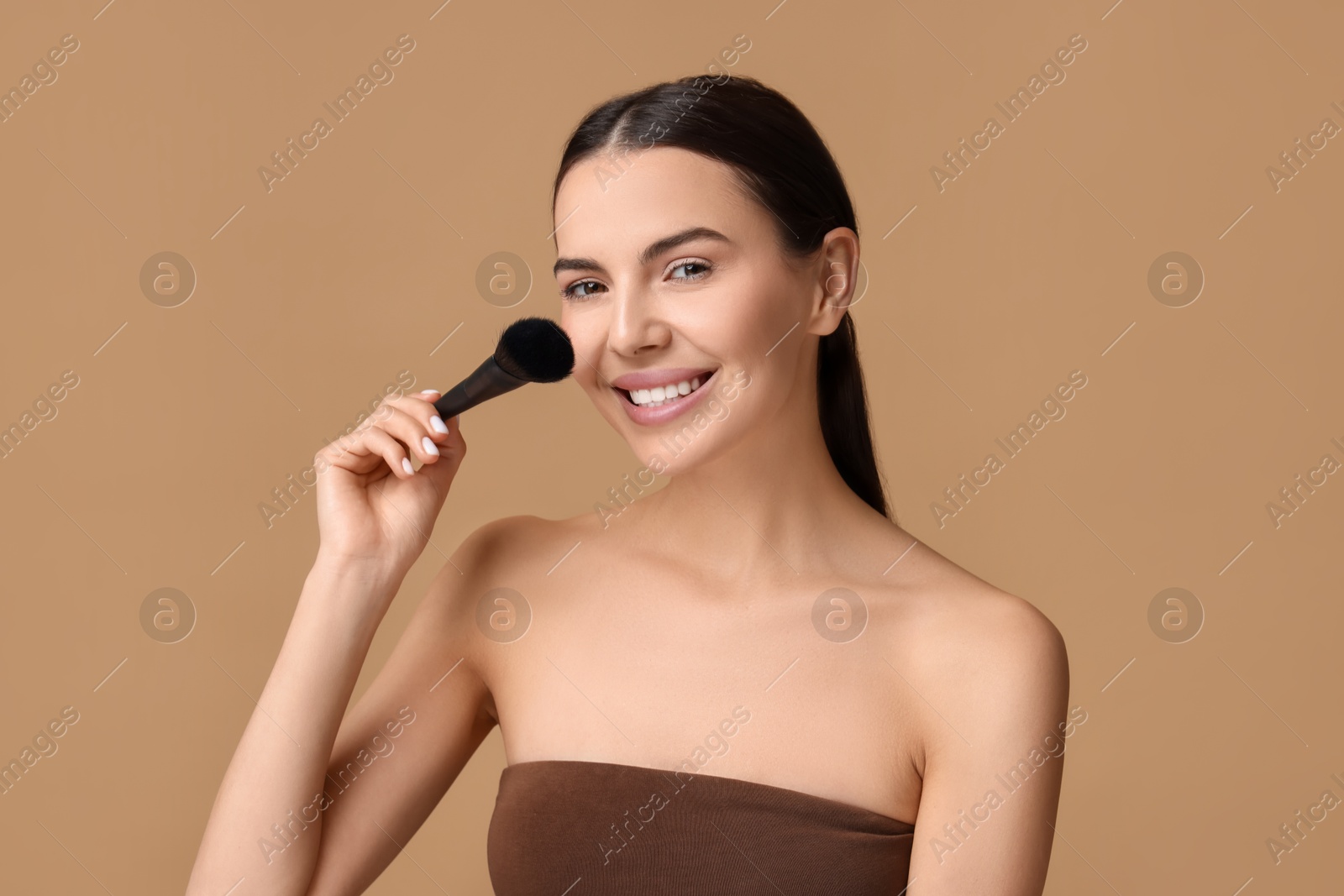 Photo of Beautiful makeup. Smiling woman with brush on beige background