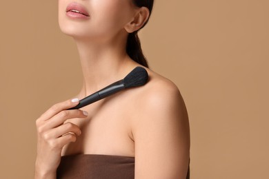 Woman with makeup brush on beige background, closeup. Space for text