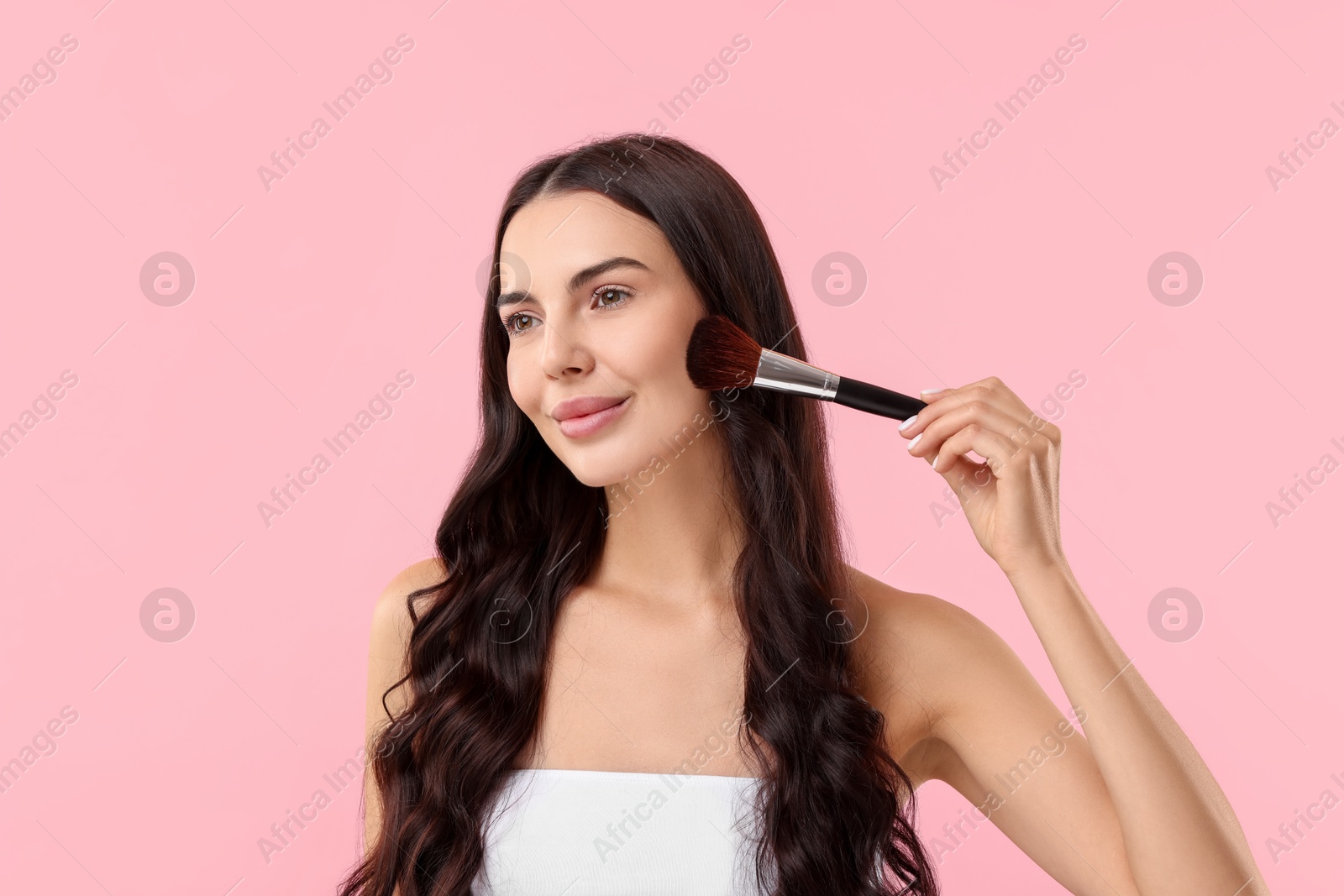 Photo of Attractive woman applying makeup with brush on pink background