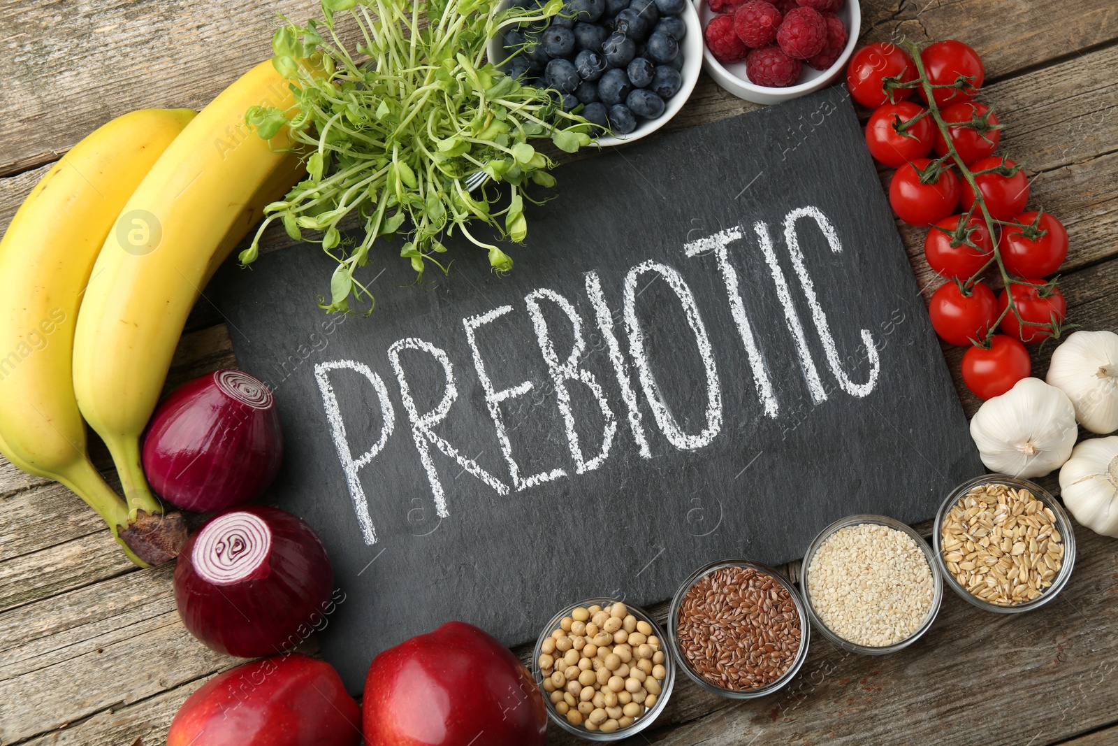 Photo of Slate board with word Prebiotic and different products on wooden table, flat lay