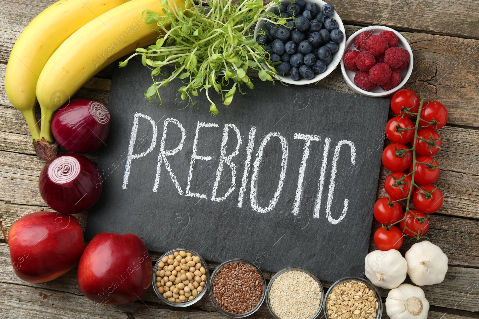 Photo of Slate board with word Prebiotic and different products on wooden table, flat lay