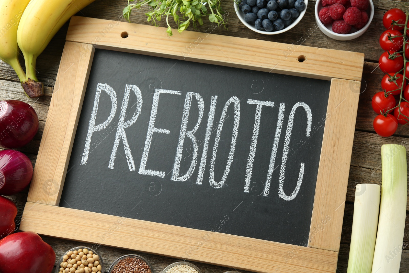 Photo of Chalkboard with word Prebiotic and different products on wooden table, above view