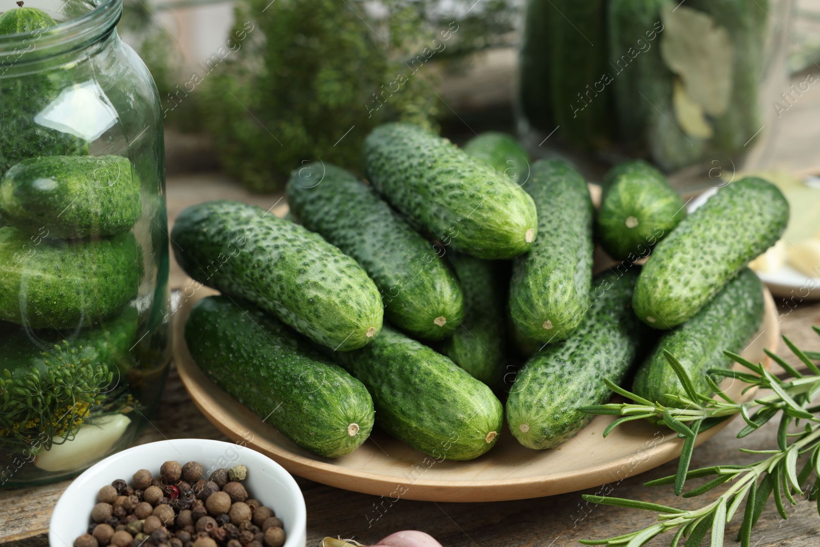 Photo of Fresh cucumbers, rosemary and peppercorns on wooden table, closeup. Preparation for pickling