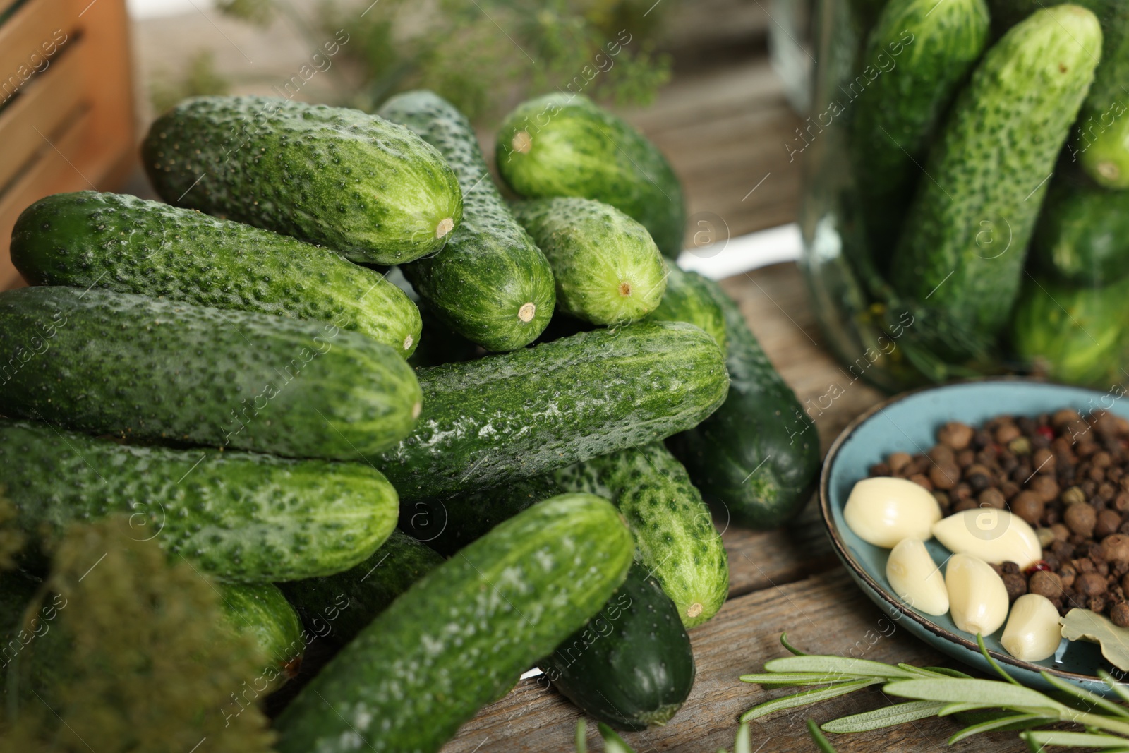 Photo of Pile of fresh cucumbers and spices on wooden table, closeup. Preparation for pickling