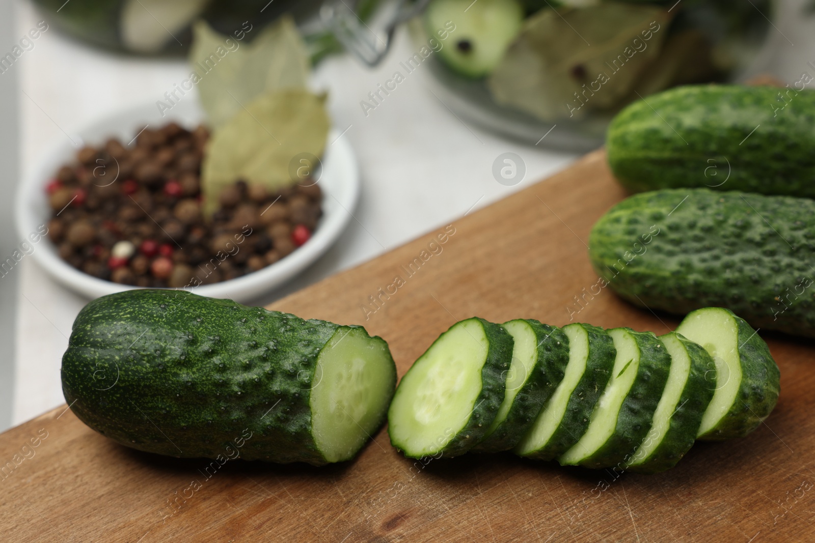 Photo of Board with fresh cut cucumber and spices on light table, closeup. Preparation for pickling