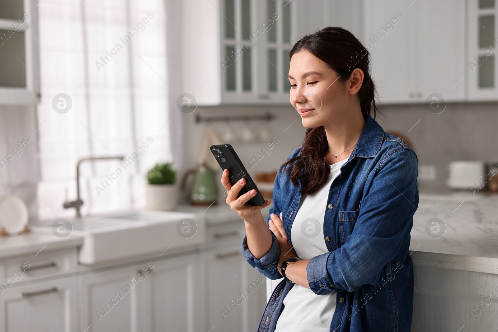 Photo of Beautiful woman using smartphone in kitchen. Space for text