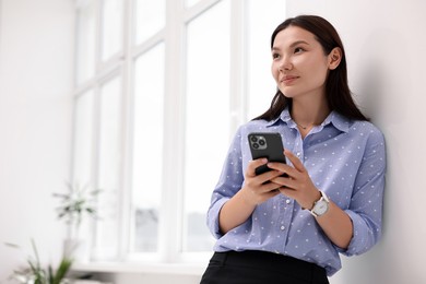 Beautiful businesswoman with smartphone in office. Space for text