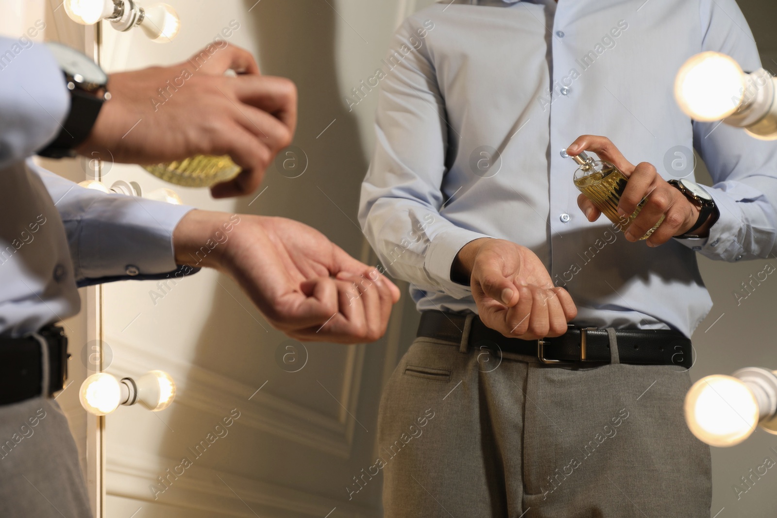 Photo of Man spraying luxury perfume near mirror indoors, closeup