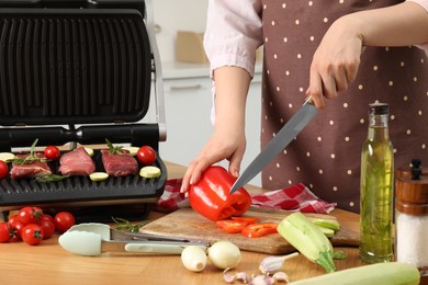 Photo of Woman cooking different products with electric grill at wooden table in kitchen, closeup