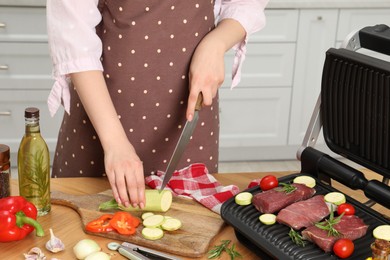 Photo of Woman cooking different products with electric grill at wooden table in kitchen, closeup