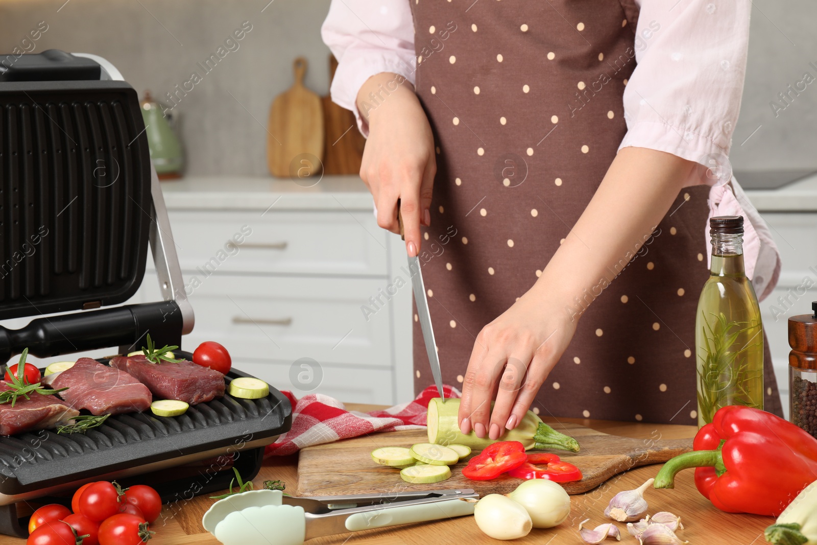 Photo of Woman cooking different products with electric grill at wooden table in kitchen, closeup