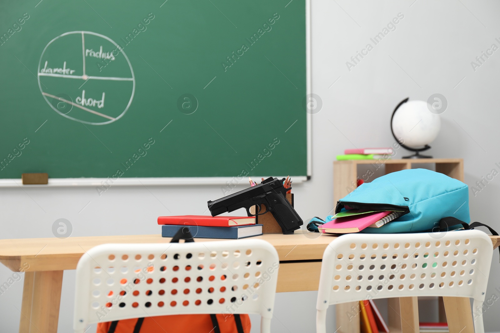 Photo of School stationery, gun and backpack on desk in classroom