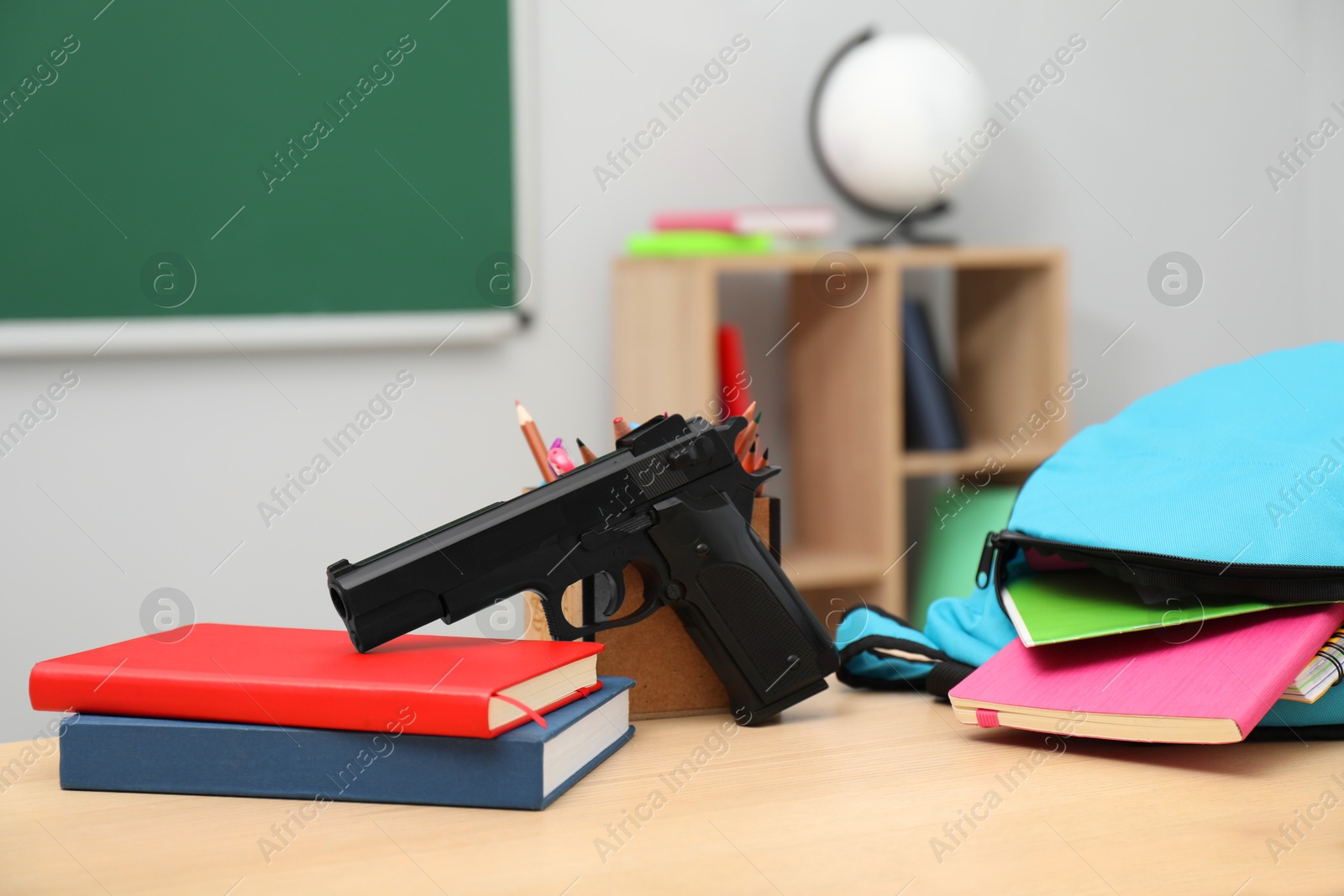 Photo of School stationery, gun and backpack on desk in classroom