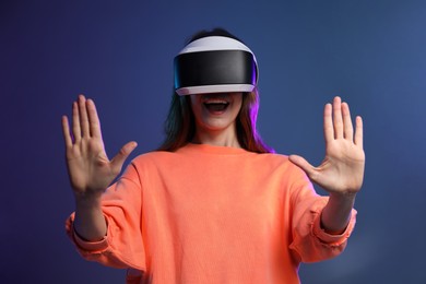 Photo of Emotional woman using virtual reality headset on dark blue background