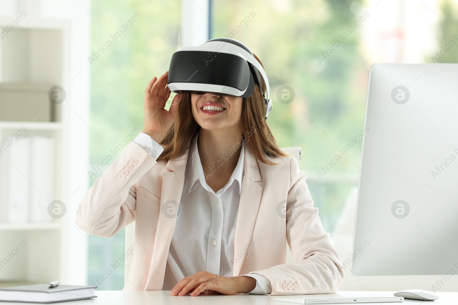 Photo of Smiling woman using virtual reality headset at workplace in office